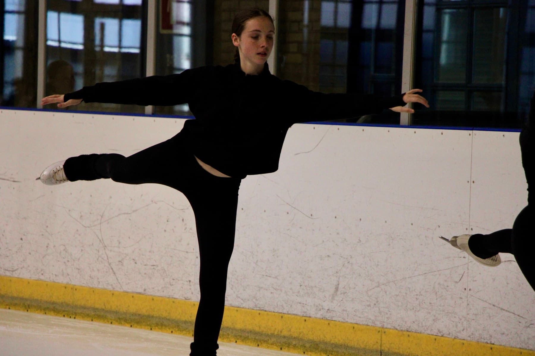 A skater training on her own in an arabesque at the boards